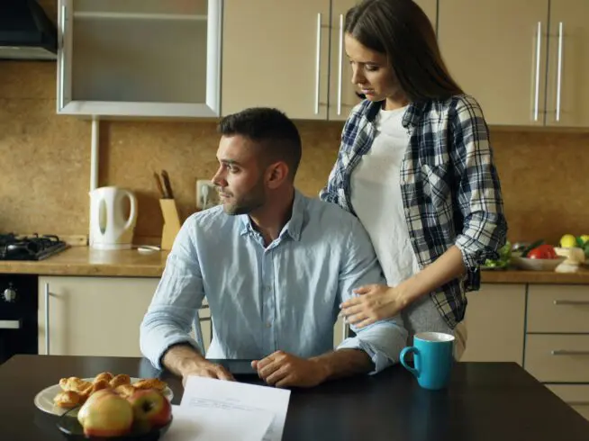 Couple sitting in the kitchen reading unpaid bills.